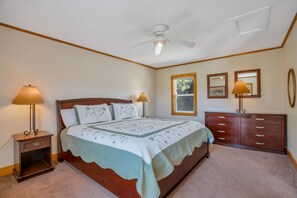 Ein Schlafzimmer mit einem Bett, Nachttischen, einer Kommode, einem Deckenventilator und zwei Wandleuchten.