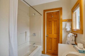 Ein Badezimmer mit einer Badewanne, einer Holztür, einem Handtuchhalter und einem Spiegel.