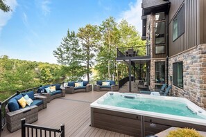 A deck with outdoor seating, a hot tub, and a stone building. - Lake House Mansion | Dock+Kayaks+FirePit+Swim Spa (Long Pond)