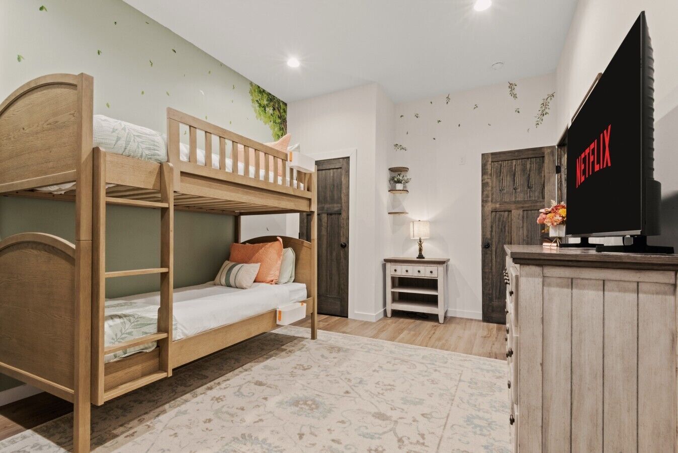 A room with bunk beds, a TV, a small table with a lamp, and a decorative wall.