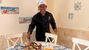 A chef standing at a round dining table with various dishes, surrounded by white chairs. - Estrella Del Mar Residence – Las Terrenas 
Beachfront 2-bedroom townhome (Las Terrenas)