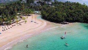A beach with clear turquoise water, a sandy shore, and a row of palm trees. - Estrella Del Mar Residence – Las Terrenas 
Beachfront 2-bedroom townhome (Las Terrenas)