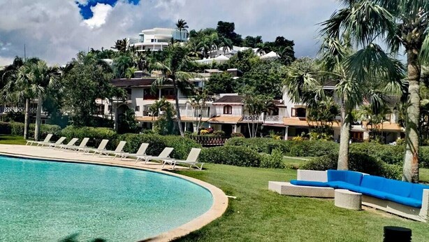 A swimming pool with lounge chairs, a blue sofa, and a view of a residential area with houses and palm trees. - Estrella Del Mar Residence – Las Terrenas 
Beachfront 2-bedroom townhome (Las Terrenas)