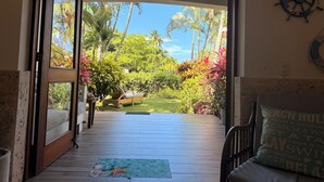 An open doorway leading to a deck with a starfish mat, a ceiling fan, and a view of a tropical garden with palm trees and colorful foliage. - Estrella Del Mar Residence – Las Terrenas 
Beachfront 2-bedroom townhome (Las Terrenas)