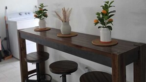 Un'area con un bancone in legno, sgabelli, un dipinto del tramonto e due piante in vaso.