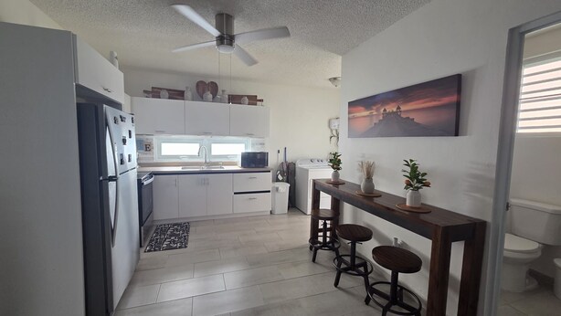 Una cucina compatta con frigorifero, microonde, lavello e ventilatore a soffitto.