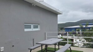 Un patio con tavolo e panche, una piccola finestra e vista su un edificio e delle colline sullo sfondo.