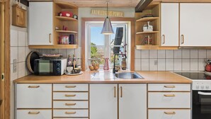 A kitchen with wooden cabinets, a microwave, a sink, and a window with a view. - Renovated townhouse in Old Tejn, Bornholm (Allinge)