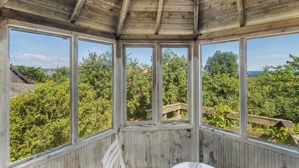 A wooden room with large windows, a wooden ceiling, and a view of greenery outside. - Renovated townhouse in Old Tejn, Bornholm (Allinge)