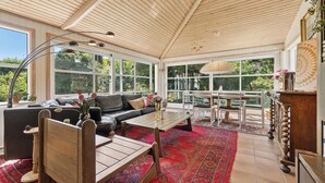 A sunroom with a wooden ceiling, large windows, a sofa, a coffee table, and a dining area. - Renovated townhouse in Old Tejn, Bornholm (Allinge)