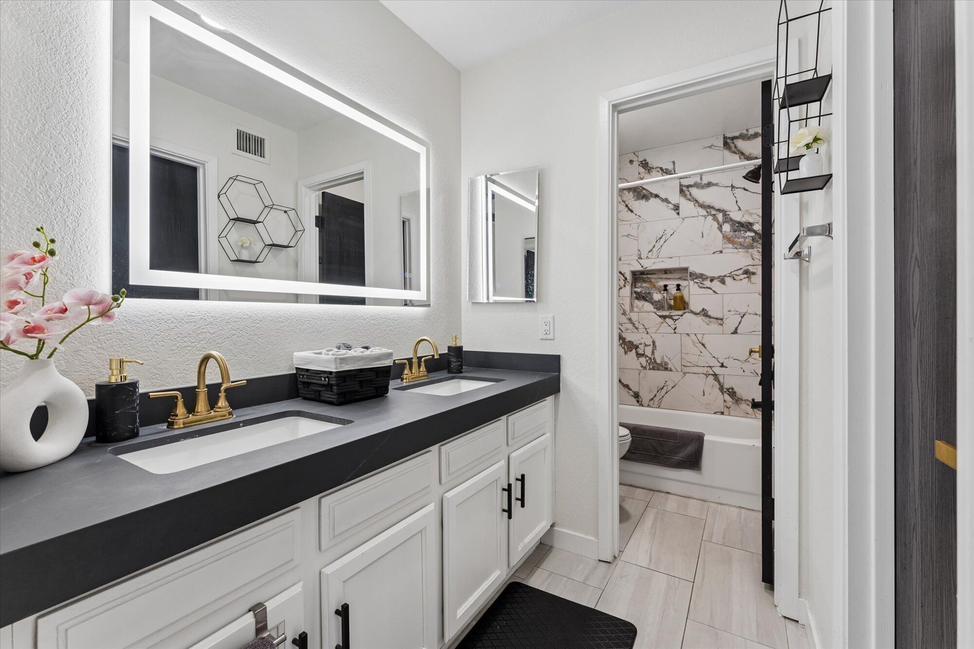 A modern bathroom with a double sink vanity, a large mirror, and a marble-tiled shower area.