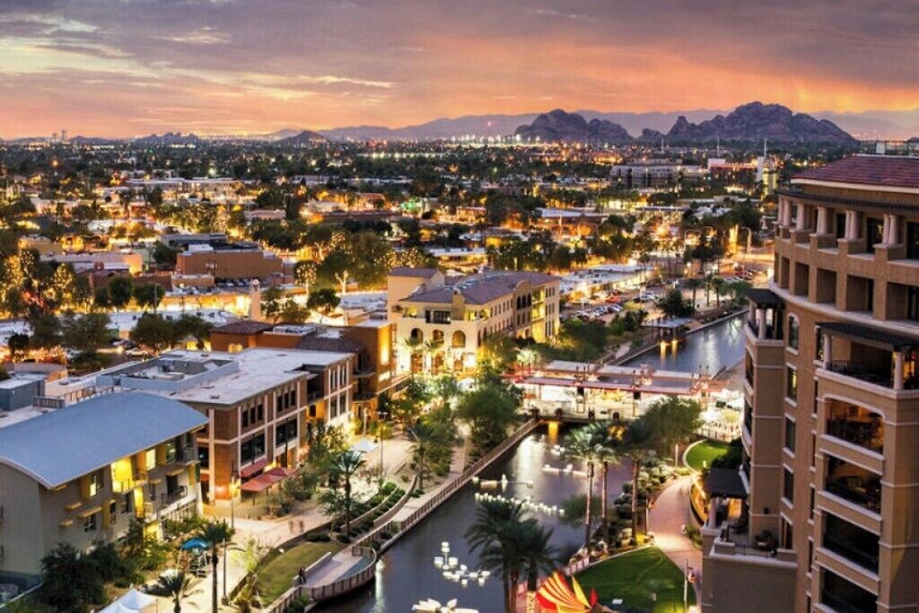 A cityscape at dusk with a river running through the center, surrounded by buildings and a mountain range in the background.