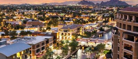 A cityscape at dusk with a river running through the center, surrounded by buildings and a mountain range in the background.
