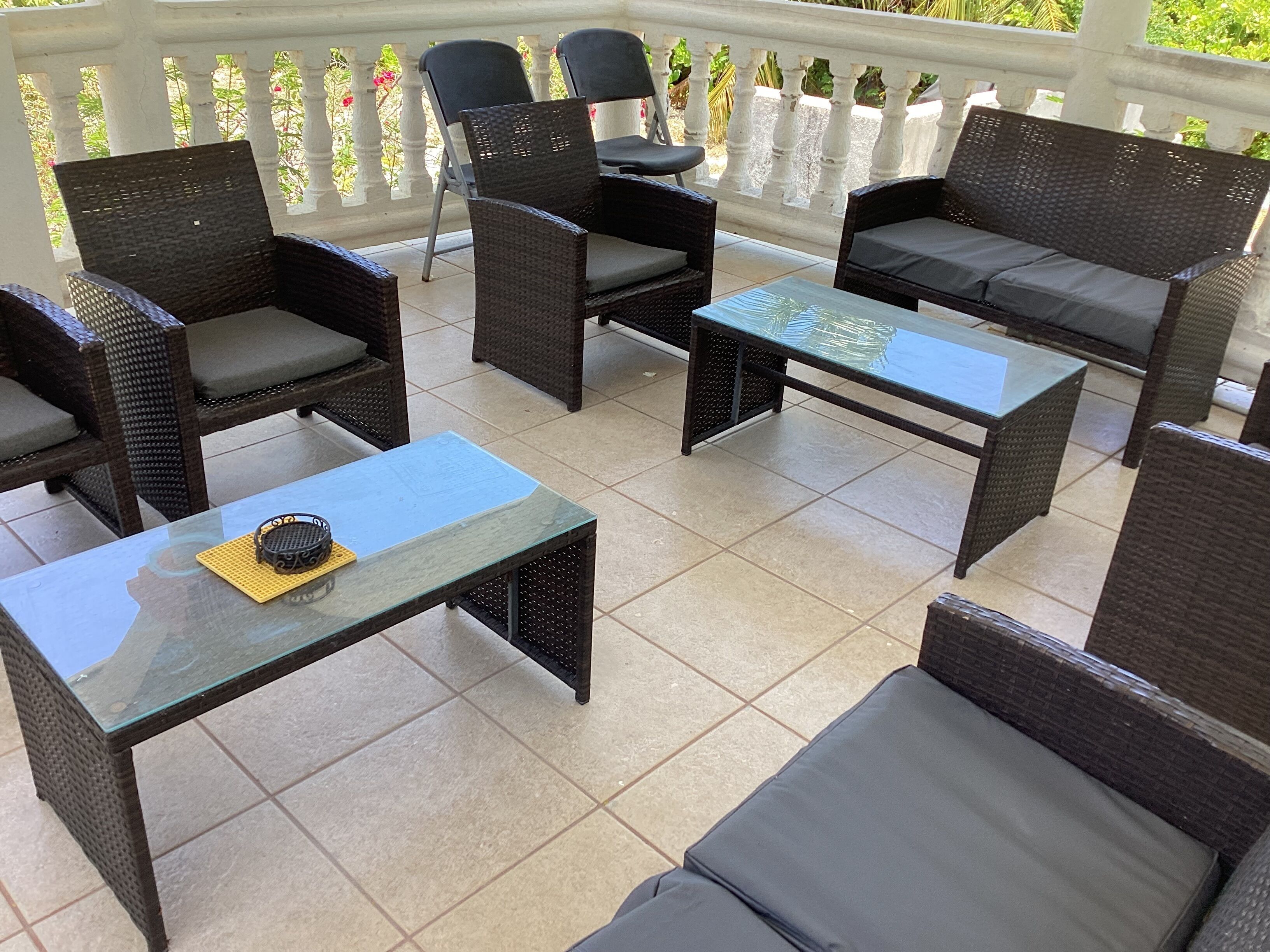 An outdoor patio with wicker furniture, including sofas and chairs, and a glass coffee table.