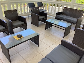 Un patio al aire libre con mobiliario de mimbre, incluyendo sofás y sillones, y una mesa de centro de vidrio.