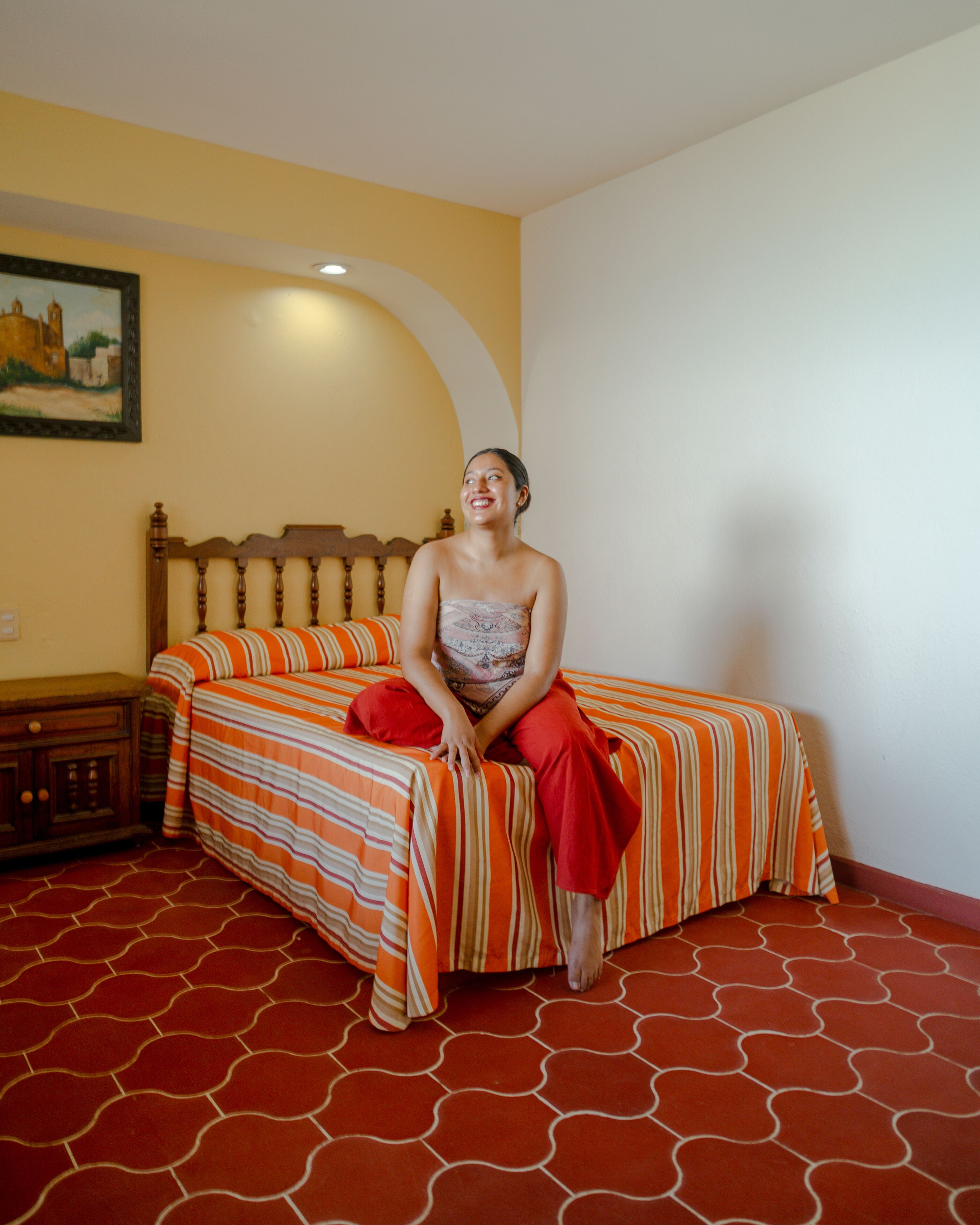 A room with a bed, a wooden headboard, a nightstand, and a wall painting.