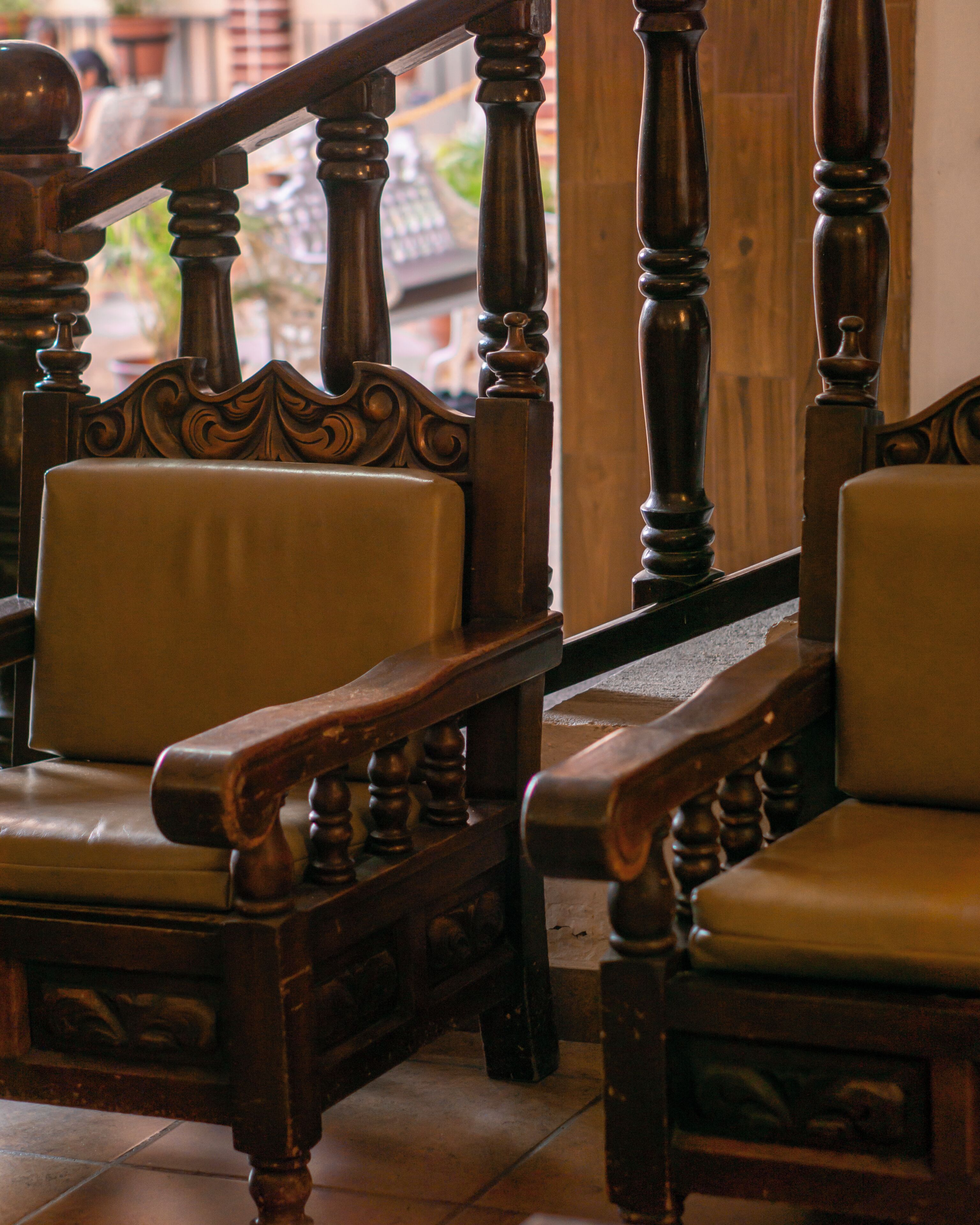 Una escalera de madera con balaustres decorativos y barandilla, que conduce a una habitación con dos sillones tapizados.
