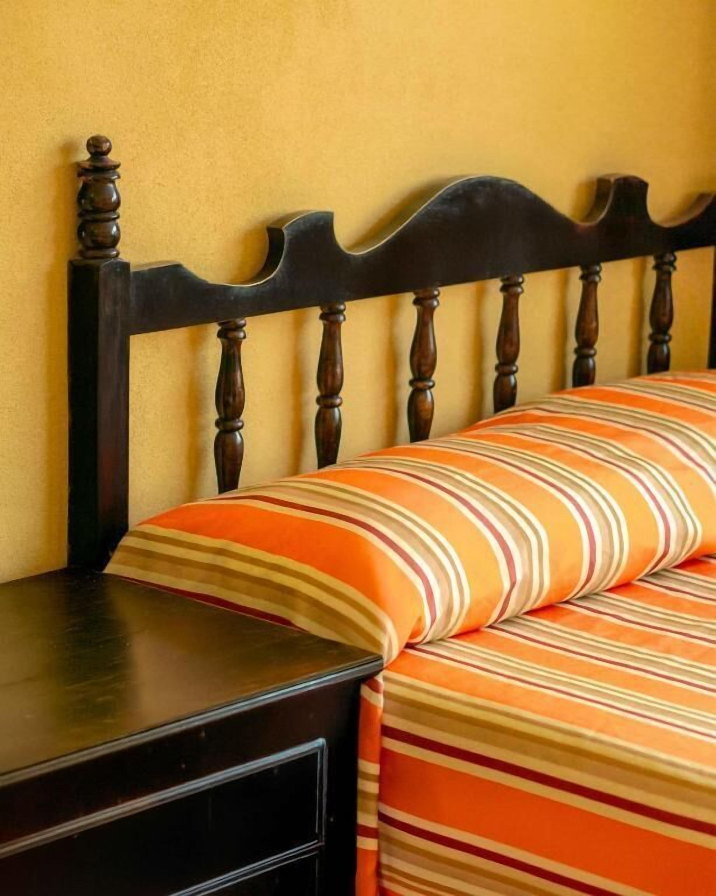 Un lit avec une tête de lit en bois et une couvre-lit rayée orange et blanche.