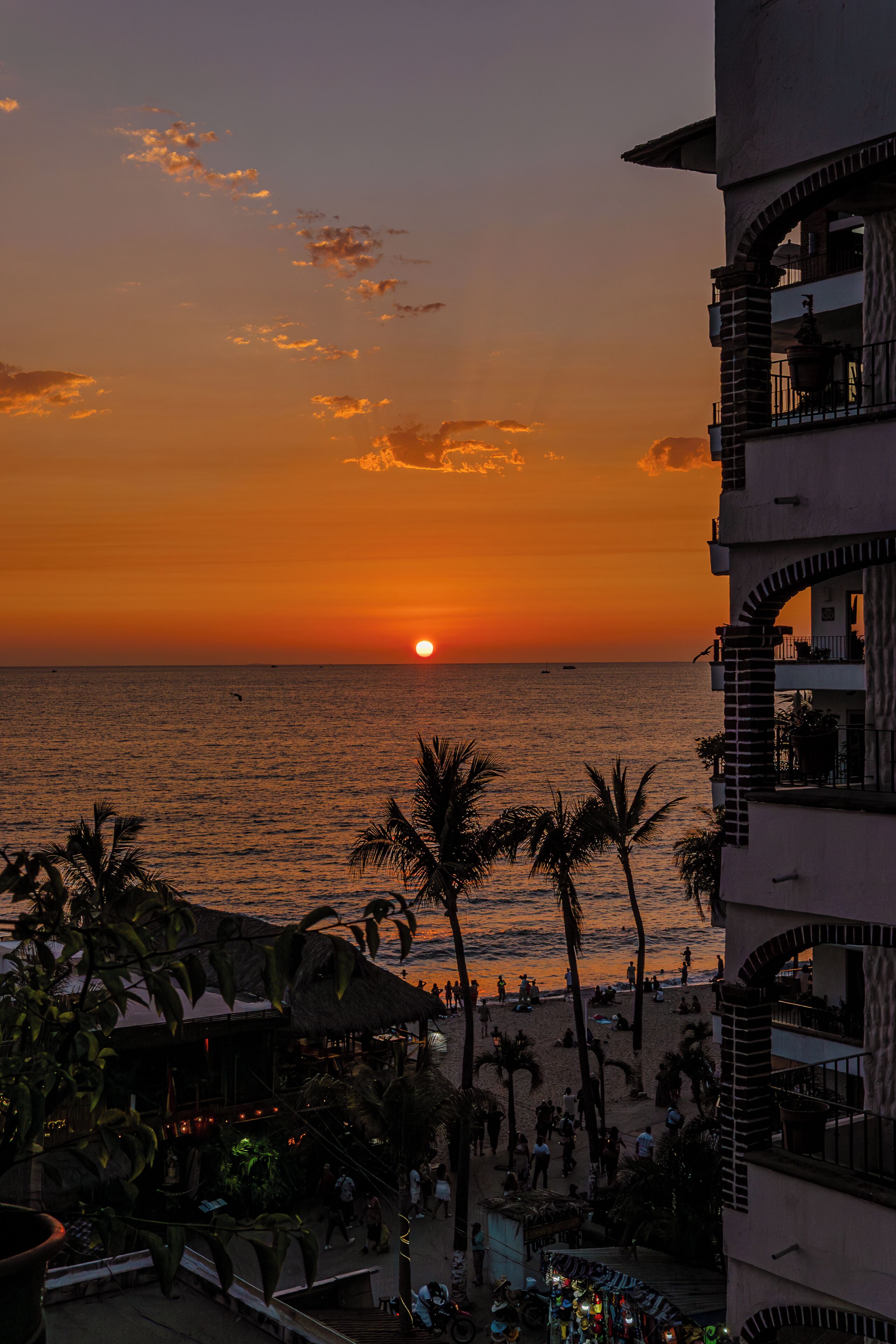 Vista al tramonto da un balcone d'hotel con spiaggia, palme e cielo sereno.