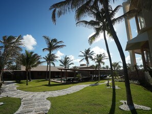 A resort with a paved walkway, palm trees, and a building with a tiled roof. - Beach front One Bedroom with Pool and Garden Views (Caponga)