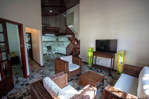 A spacious living area with wicker furniture, a television, and a staircase leading to an upper level. - Beach front One Bedroom with Pool and Garden Views (Caponga)