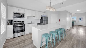 Een moderne keuken met witte kastjes, roestvrijstalen apparatuur en een centraal eiland met barkrukken.