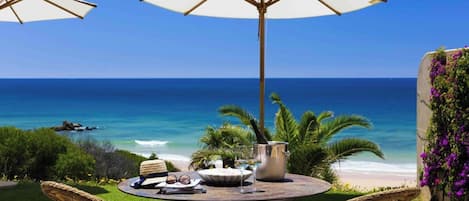 A round table with two wicker chairs, a white umbrella, and a bottle of champagne.