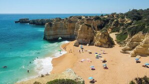 A coastal beach with clear turquoise waters, rocky cliffs, and people sunbathing on the sand. - Beach villa with ocean view and rooftop cinema (Guia)