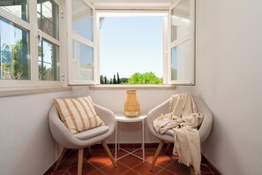 Ein Eckzimmer mit zwei Sesseln, einem kleinen Tisch und Blick durch ein offenes Fenster.