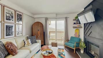 En moderne stue med sofa, sofabord, pejs og en balkon med gardiner.