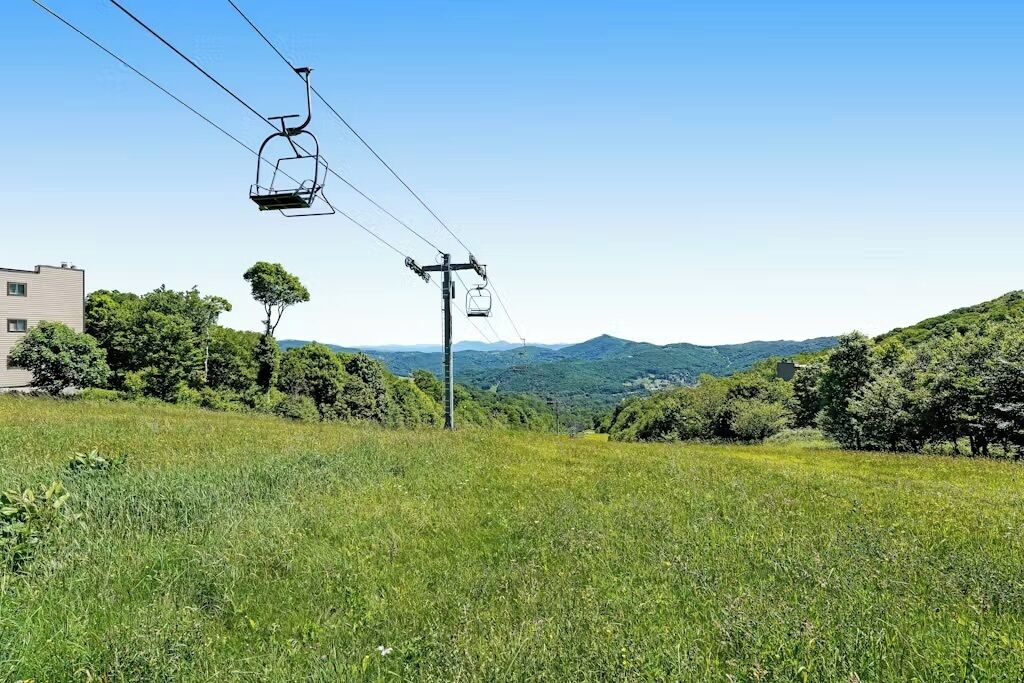 A cable car system in a hilly area with greenery and distant mountains.