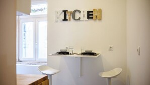 Una cucina con un cartello che riporta la scritta 'KITCHEN', due sgabelli bianchi e una finestra vista un edificio.