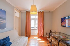 Et værelse med en seng, et bord med magasiner, en hængende lampe og et vindue med gardiner.