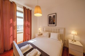 A hotel room with a bed, two bedside tables, a hanging lamp, a window with curtains, and a framed picture on the wall. - Historic Center 2-Bedroom Boutique Apartment (Lisbon)