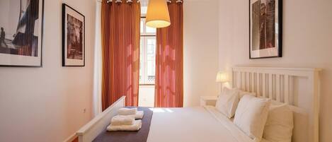 Ein Hotelzimmer mit Bett, Nachttisch, Lampe und Vorhängen.