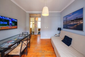 Una sala de estar con televisor, sofá, mesa de comedor y una banca.