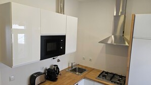 Una cucina con mobili bianchi, un forno a microonde nero, un lavello in acciaio inossidabile, un fornello a gas e una macchina da caffè.