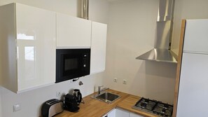 Eine Küche mit weißen Schränken, einer schwarzen Mikrowelle, einer Spüle aus Edelstahl, einem Gasherd und einer Kaffeemaschine.