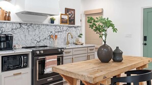 Una cocina con encimera de mármol, una mesa de madera, estufa, microondas y fregadero.