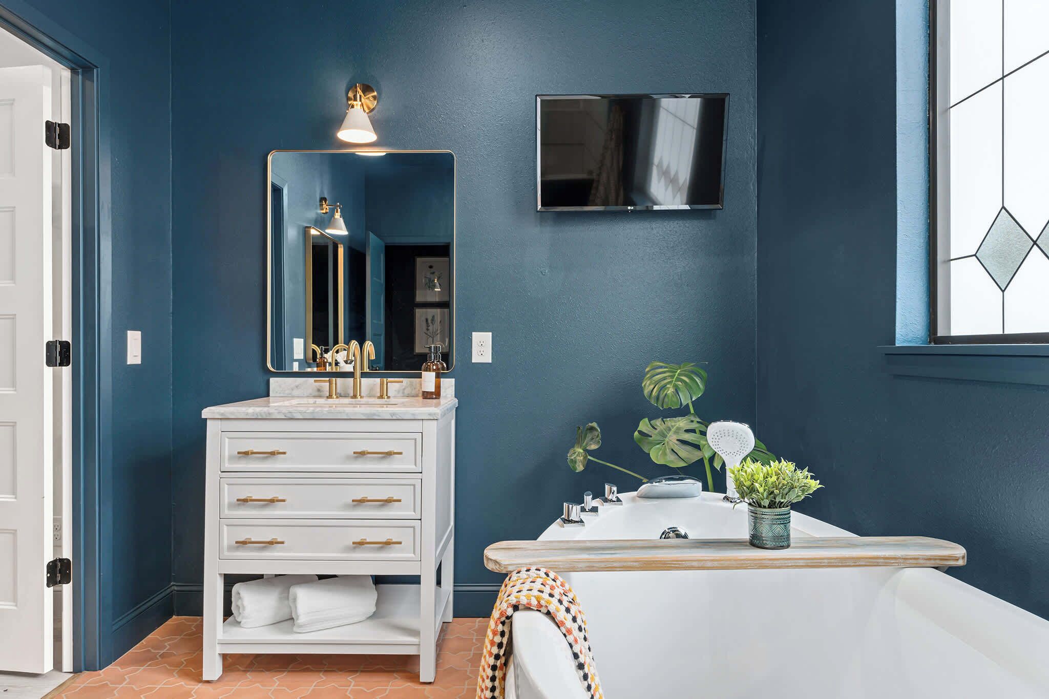 A bathroom with a white vanity, a large mirror, a mounted TV, and a window with a geometric pattern.