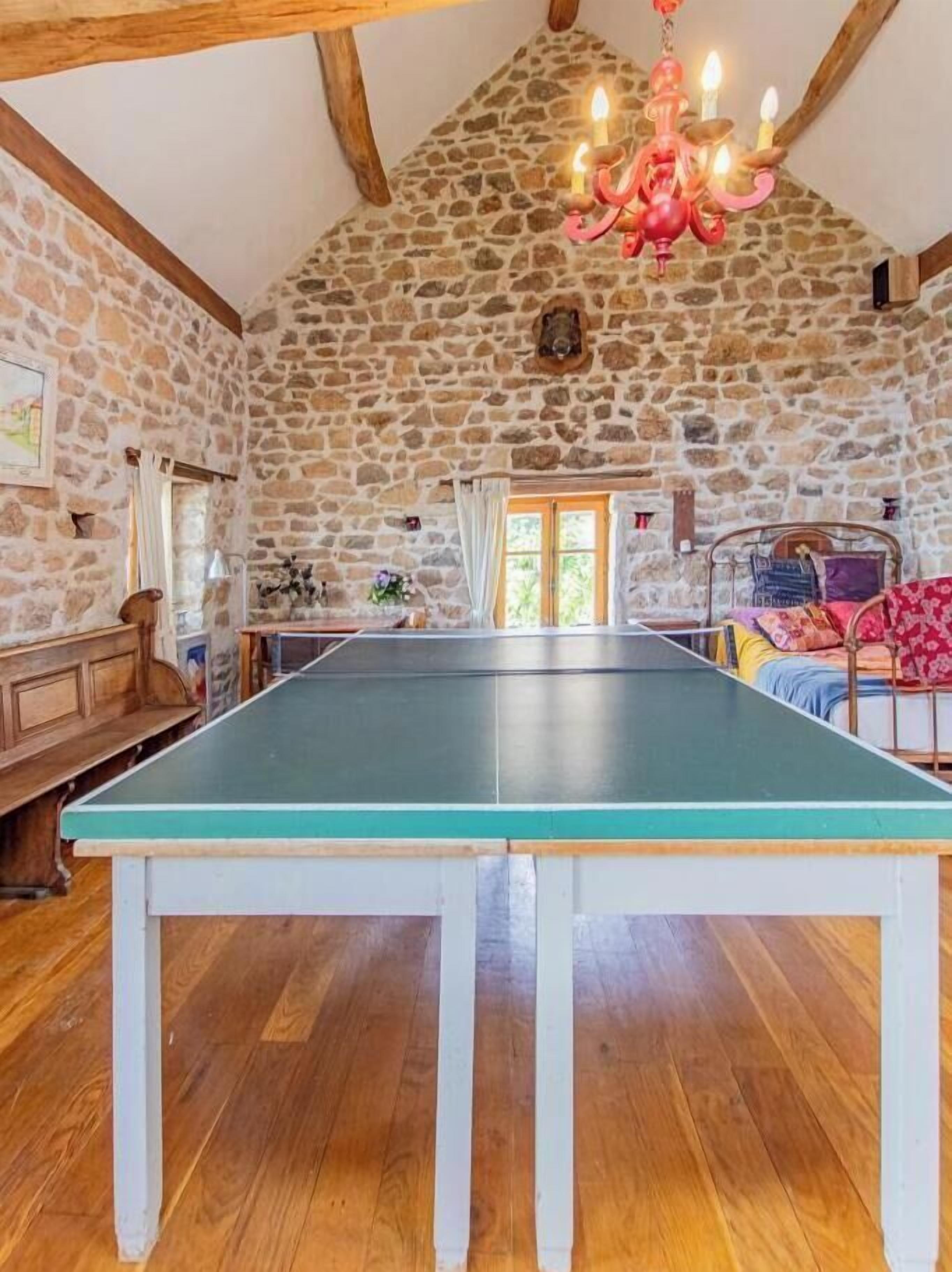 A room with a ping pong table, stone walls, wooden beams, and a chandelier.