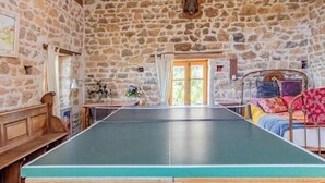 Ein Raum mit Tischtennisplatte, Steinwänden, Holzbalken und einer Chandelier.