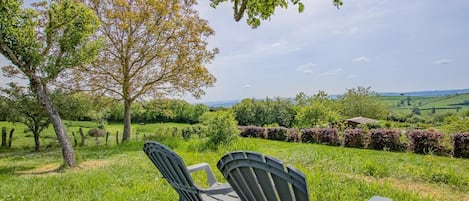 Two outdoor chairs facing a scenic landscape with a tree and a view of rolling hills.