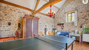 Ein Raum mit Tischtennisplatte, Steinwänden, Holzbalken, einer Chandelierleuchtre und einem fenster mit Vorhängen.