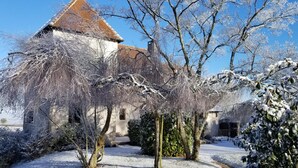 Un edificio cubierto de nieve con un techo característico, rodeado de árboles desnudos y un terreno nevado.