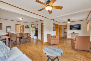 A spacious living area with a wooden floor, a ceiling fan, a television, and a dining area with chairs and a table. - 2 Bedroom Cabin near Trout Pond with Private Hot Tub (Estes Park)