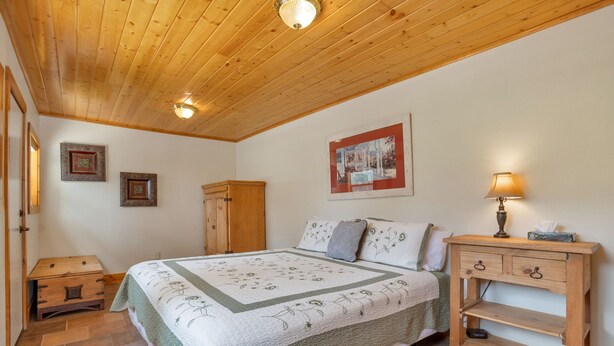 Une chambre à coucher avec un plafond en bois, un lit recouvert d’une courtepointe, une table de chevet, une armoire et un tableau encadré accroché au mur.