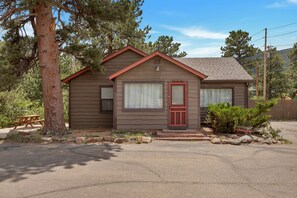 A single-story cabin with a red door, a small porch, and a wooden deck. - 2 Bedroom Cabin near Trout Pond with Private Hot Tub (Estes Park)
