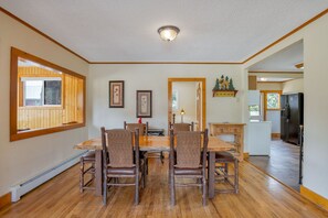 A dining area with a wooden table and chairs, a ceiling light, framed pictures on the wall, and a view of the kitchen. - 2 Bedroom Cabin near Trout Pond with Private Hot Tub (Estes Park)