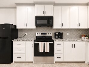 A kitchen with white cabinets, a black refrigerator, a microwave, a stove, and a coffee maker.